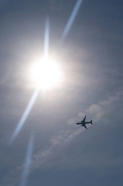 An airplane from below with lots of sky and bright sun clipart