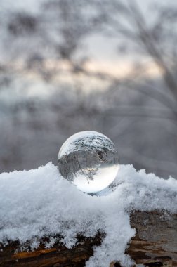 Glass ball lying in the snow on a cold winter day, with reflections of snow-covered landscape in the glass clipart