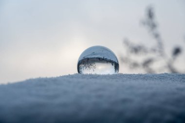 Soğuk bir kış gününde kar altında yatan cam top, camda karla kaplı manzaranın yansımaları.