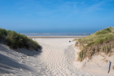 Hollanda 'daki Kuzey Denizi kıyısında, deniz kenarındaki kumulların üzerinde mavi bir gökyüzü var.