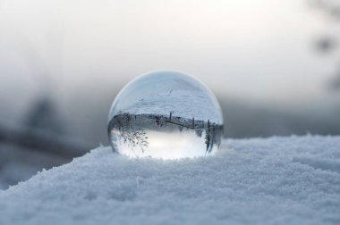 Soğuk bir kış gününde kar altında yatan cam top, camda karla kaplı manzaranın yansımaları.