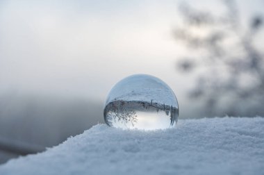 Soğuk bir kış gününde kar altında yatan cam top, camda karla kaplı manzaranın yansımaları.