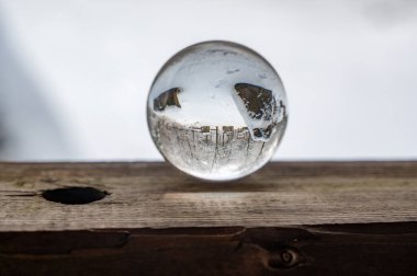 Glass ball on a wood on a cold winter day, with reflections of trees and snow in the glass clipart