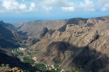 İspanya 'nın Kanarya Adası' ndaki vadide küçük bir köye sahip dağlar. Mavi gökyüzü ve bulutlarla kaplı.