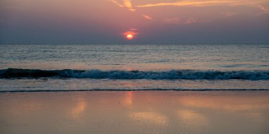 Denizin üzerinde kızıl güneşli, dalgalı ve kumlu kumlu bir gün batımı