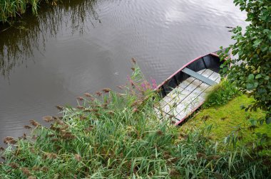 Nehrin kıyısında, suda küçük bir tekne yatıyor.