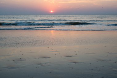 Denizin üzerinde kızıl güneşli, dalgalı ve kumlu kumlu bir gün batımı