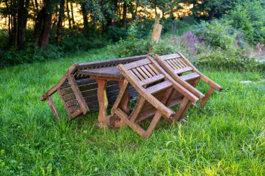 Sandalyeler ve yeşil bahçedeki ahşap masaya yaslanmış bir bank.