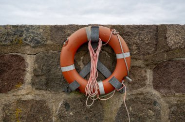 An orange lifebuoy hangs on a harbor wall clipart