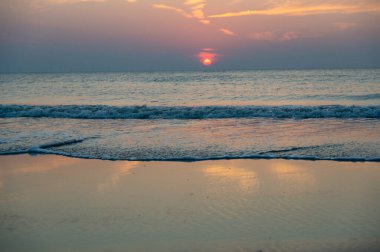 Denizin üzerinde kızıl güneşli, dalgalı ve kumlu kumlu bir gün batımı