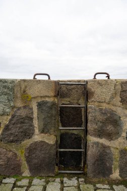 Old access ladder bolted to a harbor wall, screwed handles on the wall, with overcast sky clipart