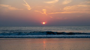Denizin üzerinde kızıl güneşli, dalgalı ve kumlu kumlu bir gün batımı
