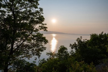 Hırvatistan, Avrupa 'da denizde gün batımı, arka planda Krk adası ve önde ağaçlar