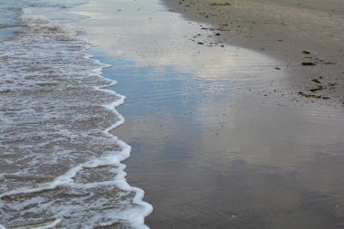 Gökyüzü kumsaldaki suya yansıyor, kumlar ve dalgalar denizde