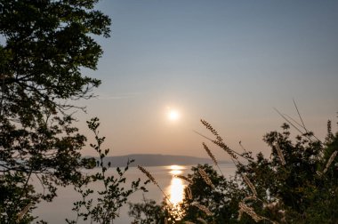 Hırvatistan, Avrupa 'da denizde gün batımı, arka planda Krk adası, önde bitki ve ağaçlar