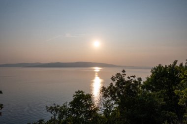 Hırvatistan, Avrupa 'da denizde gün batımı, arka planda Krk adası ve önde ağaçlar