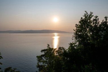Hırvatistan, Avrupa 'da denizde gün batımı, arka planda Krk adası ve önde ağaçlar