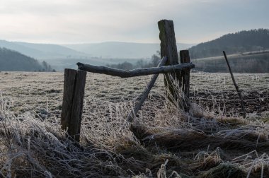 Sabahın erken saatlerinde, soğuk bir kış gününde çitin dikenli telleri çayırda donuyor.