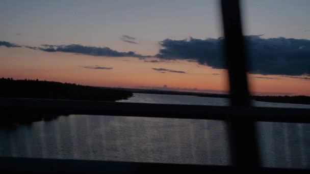 日没時に川の車の窓からの眺め 車は日没時に橋を渡って川を渡る 夏のロードトリップ 自動旅行 — ストック動画