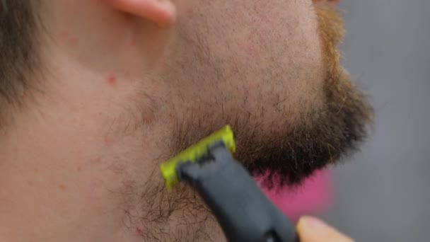 一个人用电动剃须刀刮胡子 那家伙刮掉了他的大胡子 年轻人在家里刮胡子 个人护理 — 图库视频影像