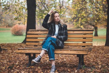 Gülümseyen esmer, sonbahar renklerinin tadını çıkararak parkın ortasında süslü bir bankta oturuyor. Sonbahar kıyafetleri içindeki gerçek bir kadının samimi portresi..