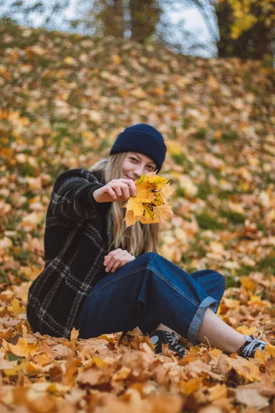 在城市公园里 坐在一堆五彩斑斓的树叶里 满脸笑容 快乐的黑发女子 秋天穿着秋装的年轻女人的肖像 — 图库照片