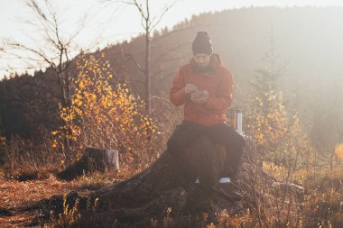 Gün doğumunda kütüğün üzerinde oturmuş lapa yiyen bir turist. Yürüyüşçüler sabah güneşiyle aydınlanır ve manzaranın tadını çıkarırlar. Beskydy Dağları, Çek Cumhuriyeti.