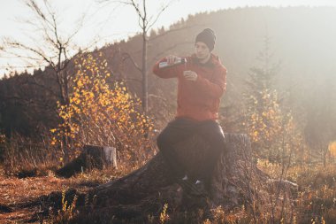 Ateşin üzerinde oturan bir turist gün doğumunda termostan bir fincana sıcak çay döküyor. Yürüyüşçüler sabah güneşiyle aydınlanır ve manzaranın tadını çıkarırlar. Beskydy Dağları, Çek Cumhuriyeti.