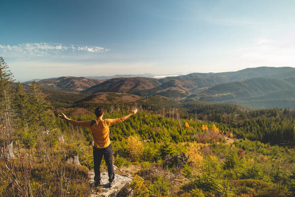 Enthusiastic traveller stands on a rock and looks down into the valley. Happy to have reached his goal. Pumping energy for the next journey. Horni Lomna, Beskydy mountains, Czech republic.