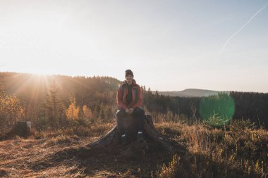 Bir kütüğün üzerinde oturan aktif yürüyüşçü gün doğumunda dağın tepesine ulaşma hissinden zevk alır. Yürüyüşçüler sabah güneşiyle aydınlanır ve manzaranın tadını çıkarırlar. Beskydy Dağları, Çek Cumhuriyeti.