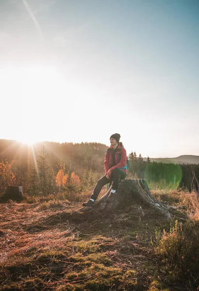 stock image Active hiker sitting on a stump enjoys the feeling of reaching the top of the mountain at sunrise. A hiker is enlightened by the morning sun and enjoys the view. Beskydy mountains, Czech Republic.