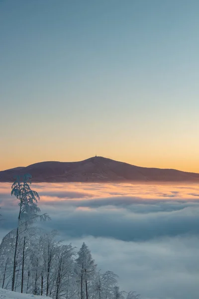 Rising Sun in the Golden Hour irradiates with its rays the impenetrable sea of clouds into orange color. Winter morning inversion. Beskydy mountains, Czech republic.