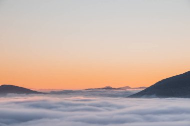Sabah güneşinin yumuşak turuncu-pembe tonunda renkli bulutlar denizi manzarası. Dağların zirveleri bu geçirmez perdeden yükseliyor. Ölümsüzlük ve mutluluk hissi. Beskydy, Çek Cumhuriyeti.