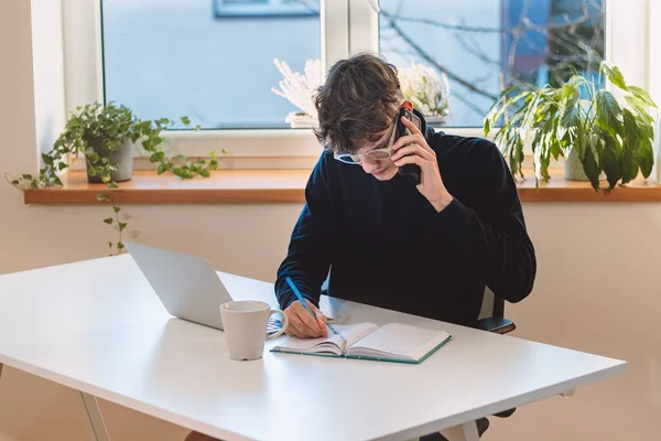 goal-oriented brown-haired businessman is on the phone with his supervisor, jotting notes in his diary. Making and arranging an appointment with a client. A young visionary in his office.