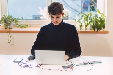 Entrepreneur in his study by the window is thinking of a new concept and strategy that will lead his company to success. A young, goal-oriented guy with glasses and brown hair.