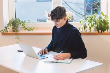 Entrepreneur in his study by the window is thinking of a new concept and strategy that will lead his company to success. A young, goal-oriented guy with glasses and brown hair.