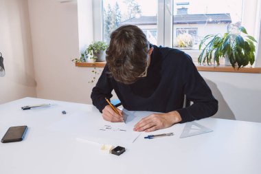 Brown-haired young architect creates new product designs for a new futuristic world. Working with your own creativity. Compass, pencil, ruler and paper. Creative home office.