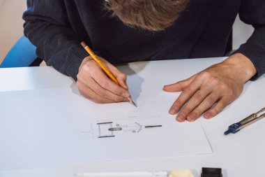 Brown-haired architect is thinking hard about how to create new product designs for a new futuristic world. He works with his own creativity. Compass, pencil, ruler and paper. Creative home office.