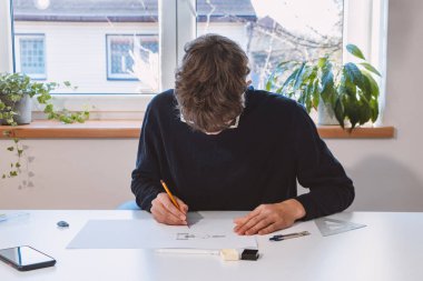 Brown-haired young architect creates new product designs for a new futuristic world. Working with your own creativity. Compass, pencil, ruler and paper. Creative home office.