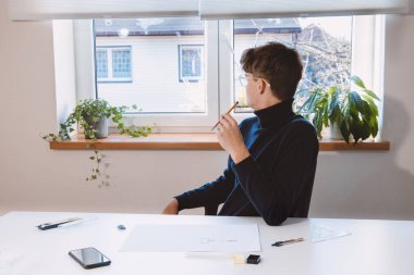 Candid portrait of an ambitious architect resting after a hard creative work and reflecting on the result of his work. Sitting contemplating his work with a smile on his lips.