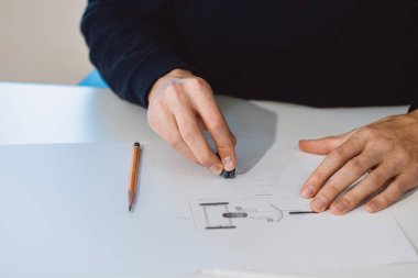 Close-up of a bright, businesslike, aspiring and young architect at his desk in his office. Drawing a new product on white paper. The work of a product designer. 