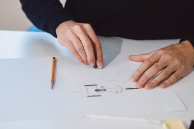 Close-up of a bright, businesslike, aspiring and young architect at his desk in his office. Drawing a new product on white paper. The work of a product designer. 