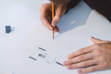 Close-up of a bright, businesslike, aspiring and young architect at his desk in his office. Drawing a new product on white paper. The work of a product designer. 