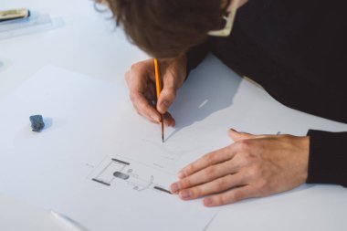 Close-up of a bright, businesslike, aspiring and young architect at his desk in his office. Drawing a new product on white paper. The work of a product designer. 