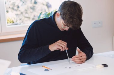Brown-haired architect is thinking hard about how to create new product designs for a new futuristic world. He works with his own creativity. Compass, pencil, ruler and paper. Creative home office.