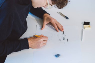 Brown-haired architect is thinking hard about how to create new product designs for a new futuristic world. He works with his own creativity. Compass, pencil, ruler and paper. Creative home office.