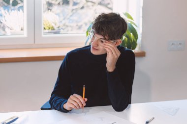 Brown-haired architect is thinking hard about how to create new product designs for a new futuristic world. He works with his own creativity. Compass, pencil, ruler and paper. Creative home office.