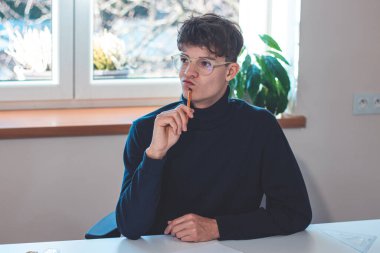 Brown-haired architect is thinking hard about how to create new product designs for a new futuristic world. He works with his own creativity. Compass, pencil, ruler and paper. Creative home office.