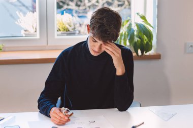 Entrepreneur and architect is thinking hard about a new design for a new prototype, which he draws in pencil on paper. Inventing a new design. An ambitious young boy. Illuminated workroom.