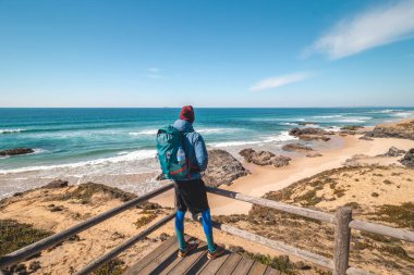 Turist, Portekiz 'in Odemira kenti Vila Nova de Milfontes yakınlarındaki Atlantik kıyısındaki kumlu bir plajda manzaranın keyfini çıkarıyor. Rota Vicentina 'nın izinden gidiyorum. Balıkçılık Yolu.